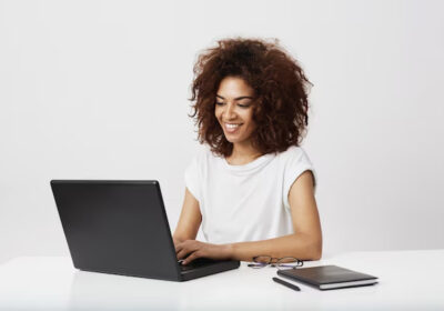 african-businesswoman-smiling-working-laptop-white-wall_176420-11190-1