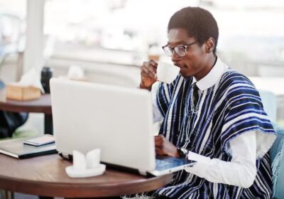 african-man-traditional-clothes-glasses-sitting-outdoor-caffe-drink-coffee-working-laptop_627829-2327