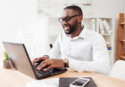 portrait-smiling-african-american-businessman-white-shirt-eyewear-sitting-working-his-laptop-office-isolated_574295-456-1-1